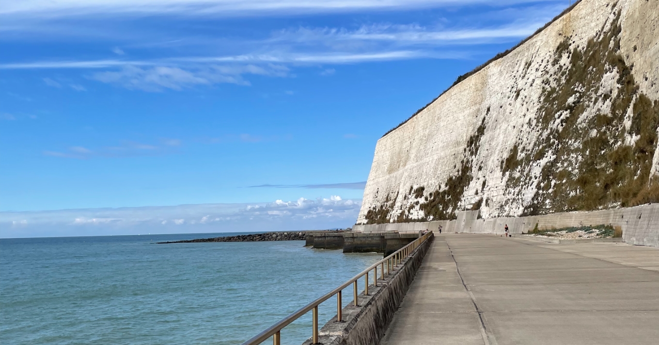 An empty promenade by the sea running into the distance under chalk cliffs