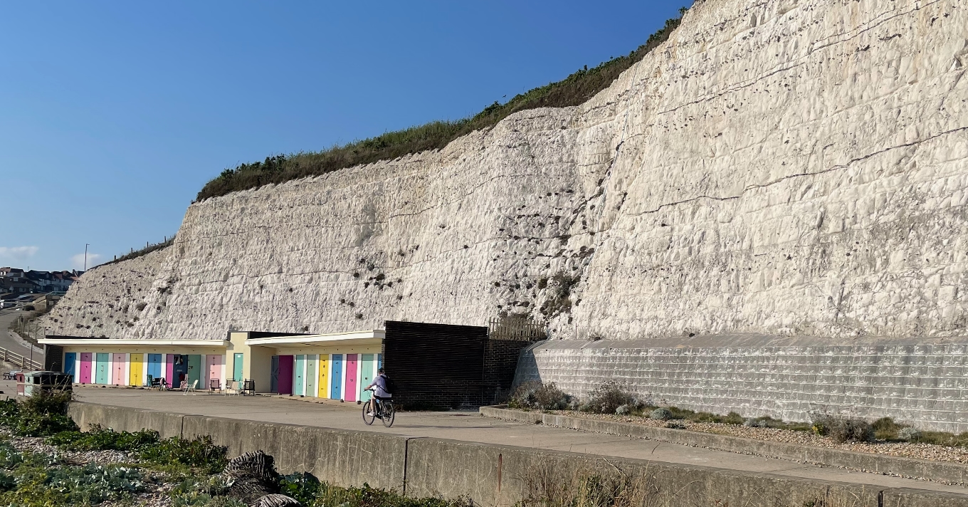 Brightly coloured beach huts at the end of a promenade under chalk cliffs